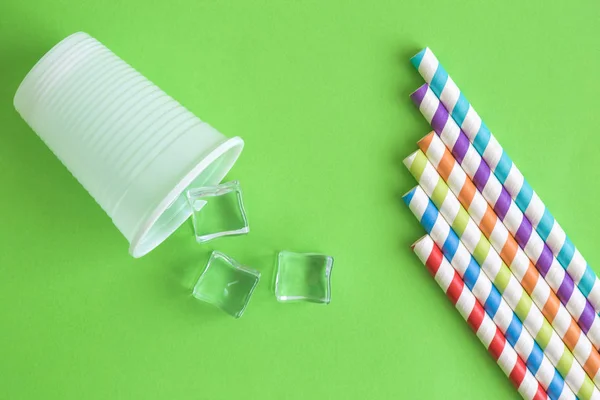 Vista superior de la taza de plástico con cubitos de hielo y pajitas de beber multicolores abstracto aislado en verde . — Foto de Stock