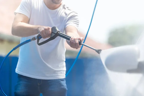 El hombre a la moda que lava el coche con el agua presurizada en el lavado de coches . — Foto de Stock