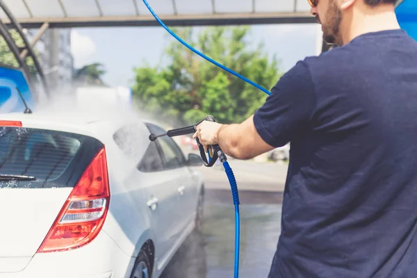 Hombre lavando su coche con agua a presión en el lavado de coches al aire libre . — Foto de Stock