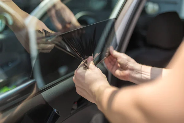 Gros plan du travailleur retirant la feuille teintée de protection solaire de la fenêtre latérale de la voiture . — Photo