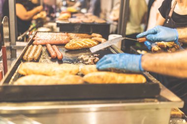 Adam sokakta profesyonel barbekü üzerinde ızgara sosis ve ısıtma çörekler eller. Fast food konsepti.