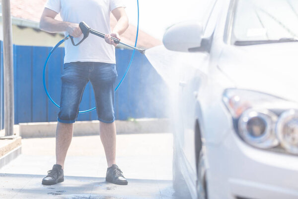 Modern man washing car with high pressure car washer spray gun