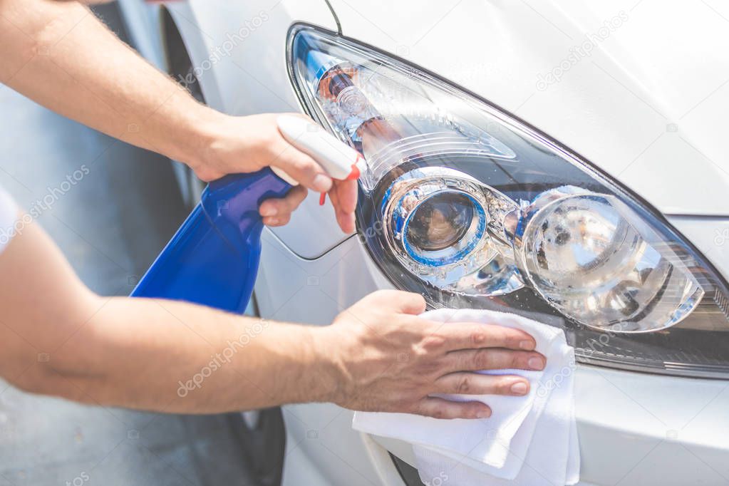 Close up of man cleaning car hood and headlights with cloth and spray bottle, car maintenance concept. Space for copy.
