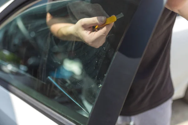 Работник, снимающий старую защитную фольгу для стекла автомобиля с бокового окна . — стоковое фото