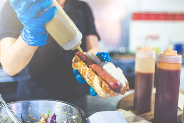 Un homme tenant un hot-dog et ajoutant de la moutarde. Rue concept de fournisseur de restauration rapide . — Photo