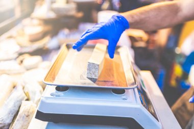 Dijital ağırlık ölçeğinde peynir parçasının ağırlığını ölçen adam.