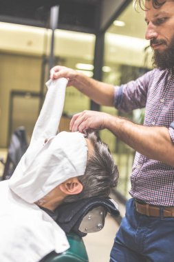 Berber ona berber dükkanında bir tıraş vermeden önce bir adam yüzüne sıcak bir havlu uygulayarak.