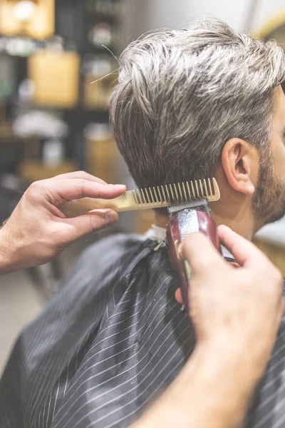 Zijaanzicht van professionele kapper styling haar van zijn cliënt met behulp van kam en Clipper. — Stockfoto