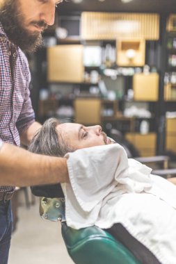 Kuaför havlu ile tıraş için müşteri hazırlanıyor. Berber dükkanını ziyaret eden adam.