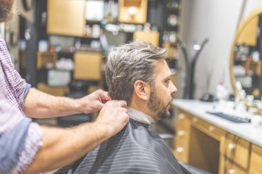 Profesyonel berber çalışmaya hazır ve berber dükkanı arka planda cape sakallı adam ile kapsayan.