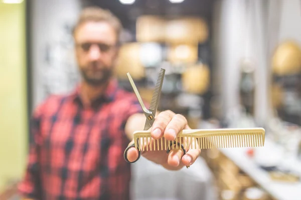 Modern man hairdresser holding sharp professional scissors and comb at barbershop. — Stock Photo, Image