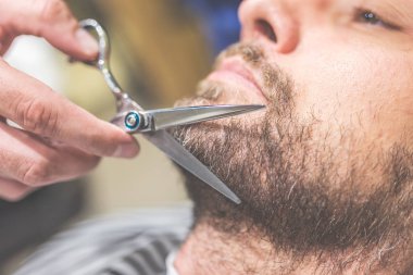 Sakal tımarı. Berber dükkanında sandalyede otururken kuaför tarafından sakal kesimi yaptıran genç sakallı adamın yan görünümü