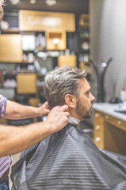 Profesyonel berber çalışmaya hazır ve berber dükkanı arka planda cape sakallı adam ile kapsayan.