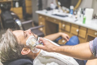 Berber dükkanında sakal tıraşı sırasında moda adam müşteri.