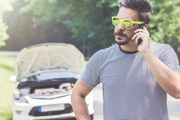 Mann telefoniert mit Handy und kaputtem Auto im Hintergrund — Stockfoto