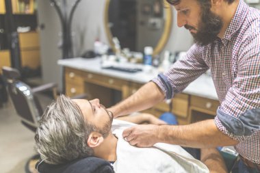 Kuaför havlu ile tıraş için müşteri hazırlanıyor. Berber dükkanını ziyaret eden adam.