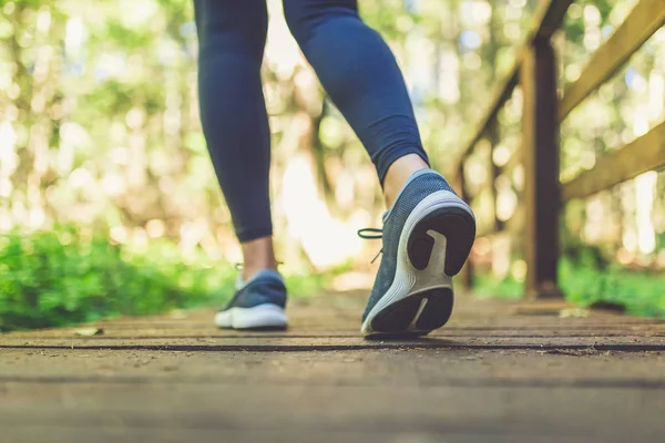 Primer plano de las piernas femeninas con zapatillas de correr en el sendero de madera en el bosque. Naturaleza y deporte concepto de estilo de vida saludable . —  Fotos de Stock