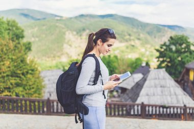 Eski dağ köyü ahşap bungalovlarının yakınlarında tablet kullanan neşeli, güzel genç bir kadın..