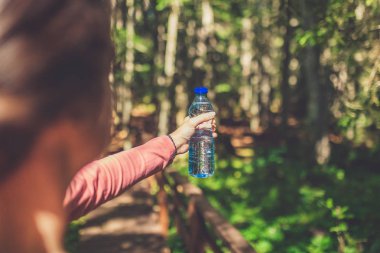 Genç bir kadının ormanda ya da parkta elinde bir şişe taze su tutarken görüntüsü. Spor ve eğlence konsepti.