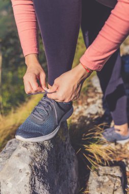 Dağların zirvesinde kayaya ayakkabı bağı bağlayan spor kadınına yaklaş. Aktif yaşam tarzı ve doğa kavramı.