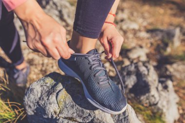 Dağların zirvesinde kayaya ayakkabı bağı bağlayan spor kadınına yaklaş. Aktif yaşam tarzı ve doğa kavramı.