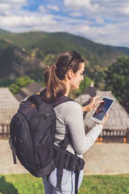 Eski dağ köyü ahşap bungalovlarının yakınlarında tablet kullanan neşeli, güzel genç bir kadın..