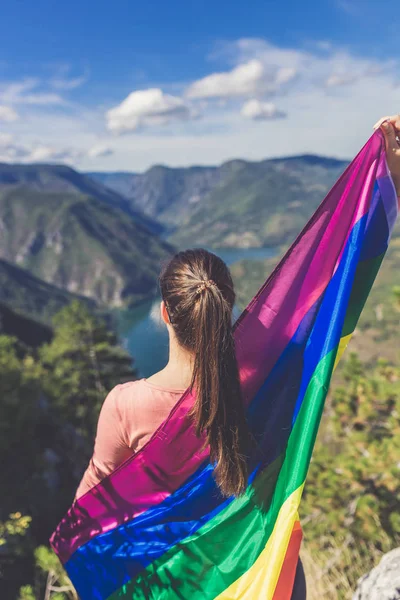 Mujer envuelta en bandera del arco iris contra hermoso paisaje de la naturaleza . — Foto de Stock