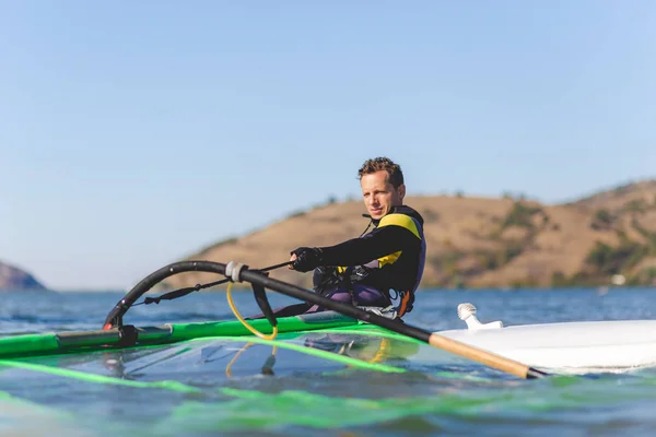 Retrato de windsurfista preparando seu equipamento enquanto sentado a bordo . — Fotografia de Stock