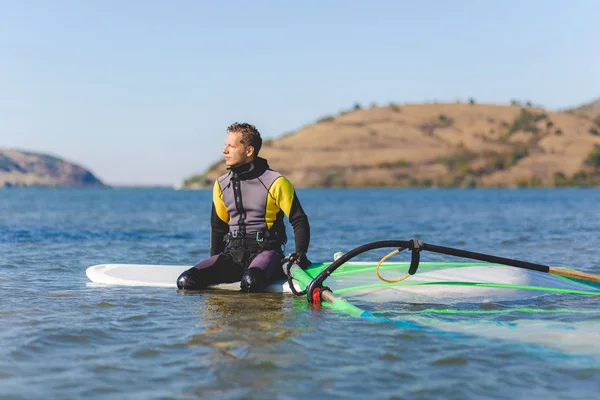 Profesionální windsurfer nosí neoprén sedí na palubě a čeká na vítr. — Stock fotografie