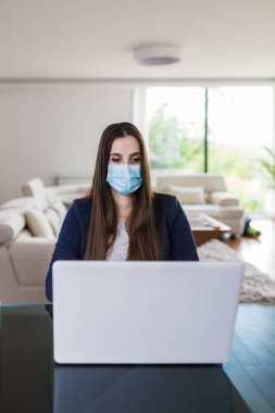 Cerrahi maskeli genç bir iş kadını evinden online olarak çalışıyor, covid-19 izolasyon kavramı..