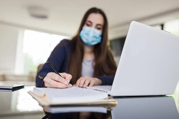 Young woman wearing medical face mask working from home. Freelancer or online learning concept during coronavirus pandemic.