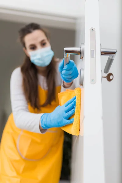 Close up of woman with protective mask cleaning door. Coronavirus prevention concept.