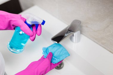 Ellerinde mikrofiber bez tutan lastik eldivenler ve lavabo musluğunu dezenfekte etmek için sprey şişesi dezenfekte eden kadın eller..