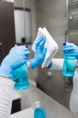 Tıbbi eldivenlerle kadın ellerini kapat aynayı bezle cilala ve dezenfektan sprey kullan. Oda servisi ve temizlik servisi..