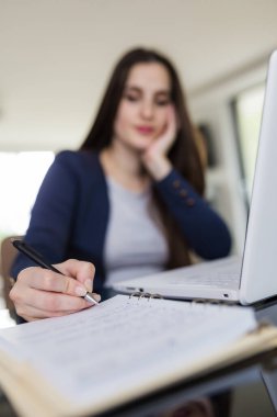 Masasında dizüstü bilgisayarının önünde oturan ve not alan genç bir kadının portresi. E-öğrenme kavramı.