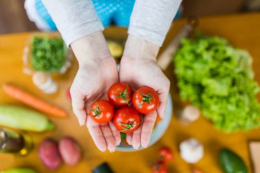 Mutfaktaki çeşitli sebzelerle dolu masaya karşı elinde kiraz domatesleri tutan kadınların yüksek açılı görüntüsü. Vejetaryen gıda konsepti.
