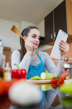 İnternette sağlıklı yemek tarifi bulmak için mutfakta dijital tablet kullanan bir kadın..