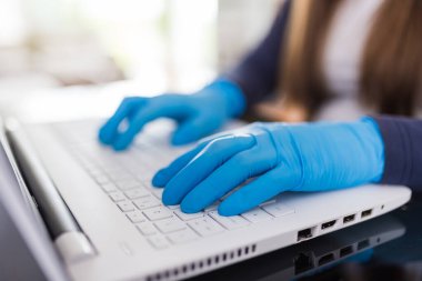 Dizüstü bilgisayarın klavyesindeki ameliyat eldivenleriyle kadın ellerini kapat. Ev yapımı covid-19 konsepti.