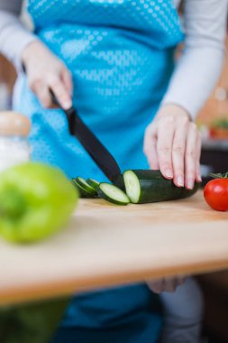 Mutfakta salatalık dilimleyen önlüklü kadına yakın çekim. Sağlıklı yemek hazırlama konsepti.