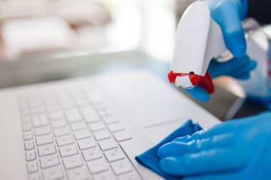 Kadın ellerini cerrahi koruyucu eldivenlerle kapatın. Laptop klavyesini mikrofiber bez ve dezenfektanla temizleyin.