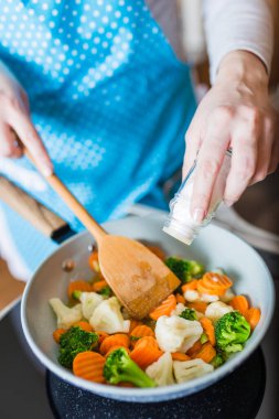 Kadının tavada karışık sebze tuzlamasına yakın çekim. Sağlıklı ev yapımı yemek hazırlama konsepti.