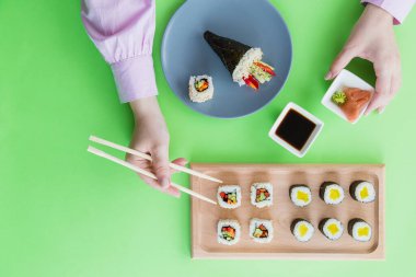 Restorandaki tabaktan suşi rulosu almak için yemek çubuğu tutan kadınların yüksek açılı görüntüsü..