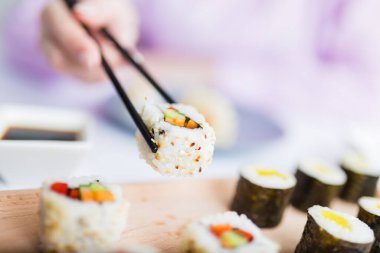 Kadın eli yemek çubuklarıyla suşi rulosu alıyor. Sağlıklı deniz ürünleri, Asya Japon yemekleri..