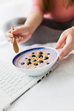 Dizüstü bilgisayarla çalışırken yaban mersinli müsli yiyen hamile kadını kapat..