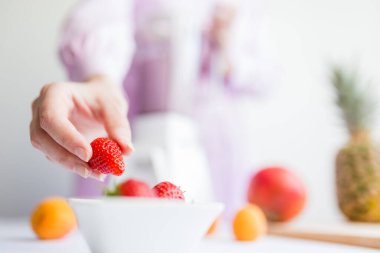 Mutfakta meyve püresi hazırlarken bir kadın çilek tutuyor..