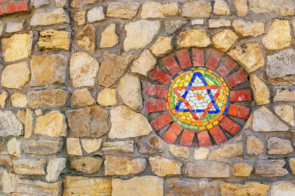 Mosaic star of David on stone wall.