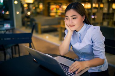 Kafede gece dizüstü bilgisayar kullanan mutlu kadın 