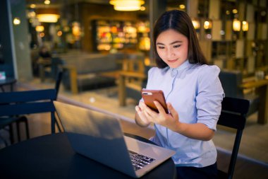 Kafede gece saatlerinde akıllı telefon kullanan mutlu kadın