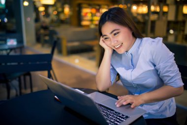 Kafede gece dizüstü bilgisayar kullanan mutlu kadın 