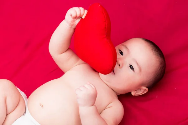 Asiático bebê com travesseiro de coração no fundo vermelho — Fotografia de Stock